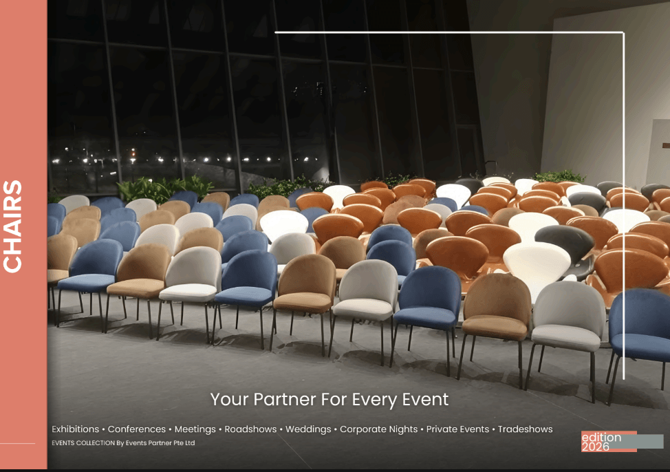 Rows of assorted colored chairs are arranged in a large, modern indoor event space with floor-to-ceiling windows at night.